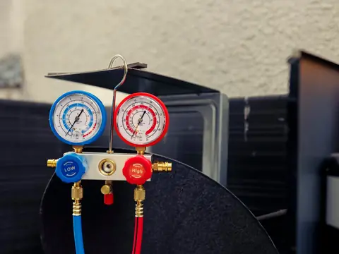 A blue low-side gauge and a red high-side gauge on a manifold with hoses attached, hung on an opened outdoor unit
